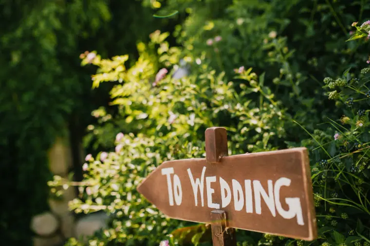 Hand-painted To Wedding sign pointing through the garden greenery