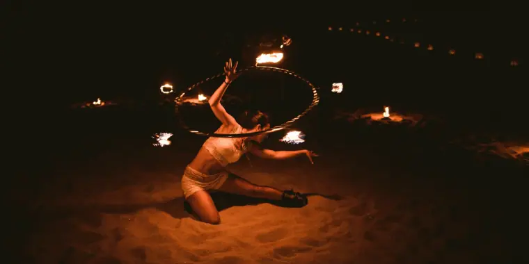 Fire performer dancing with flaming hoops on the sand at night