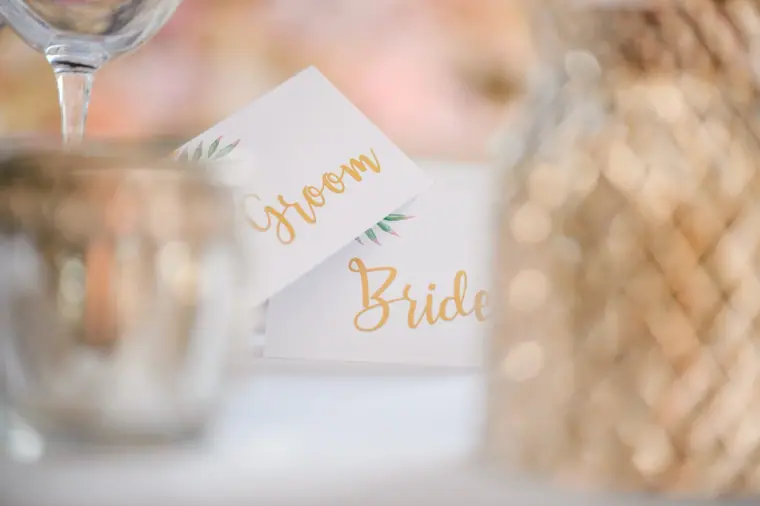 Groom and Bride place cards in gold calligraphy beside glassware on the top table