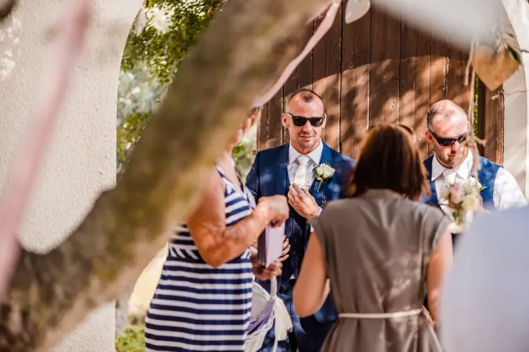 Groom in a navy suit and sunglasses greeting guests under the trees
