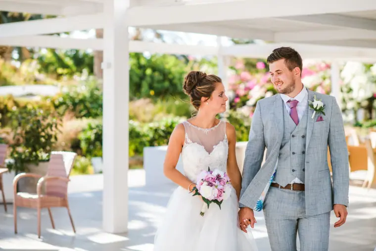 Bride and groom walking hand in hand beneath a white pergola