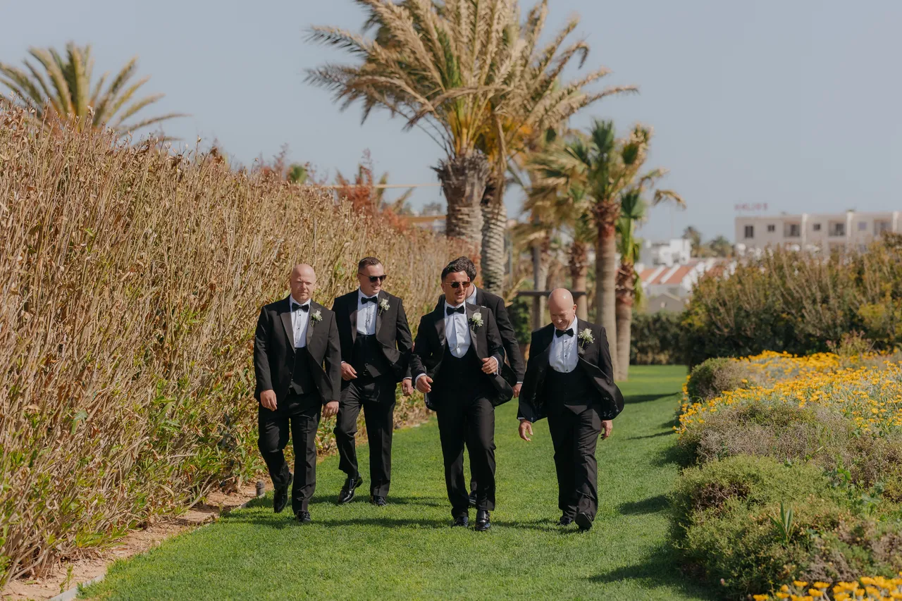 Groomsmen in tuxedos striding across the lawn towards the ceremony