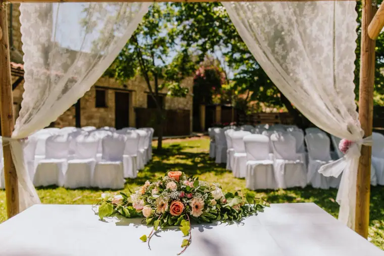 White ceremony chairs seen through lace-draped wooden frame with floral garland