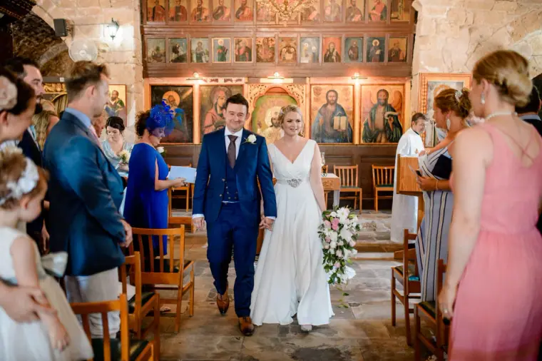 Francesca and Stephen walking back down the aisle as guests smile, Ayia Kyriaki