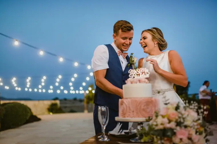 Nicola and Joel laughing as they cut the pink rose cake at dusk