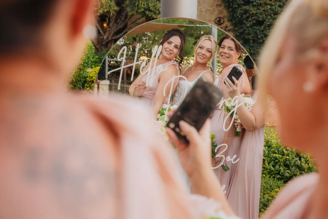 A bridesmaid taking a selfie with the others in the mirrored sign