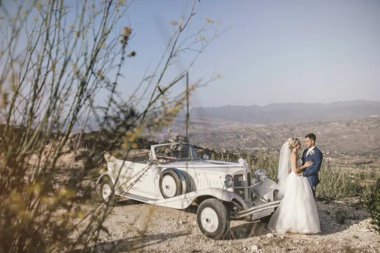 Bride and groom beside their vintage car on a hilltop overlooking the valley