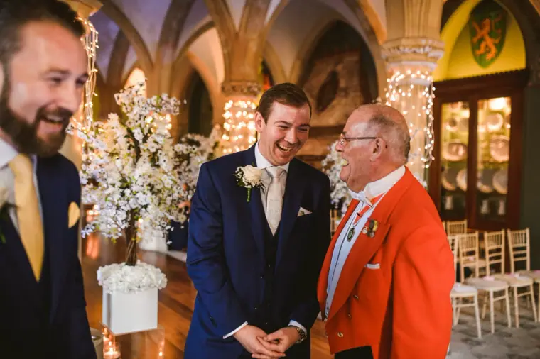 Groom laughing with his best man and a red-coated toastmaster before the ceremony