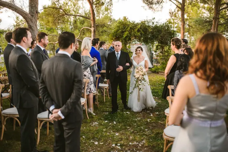 Bride walking down the grassy aisle on her father's arm past standing guests