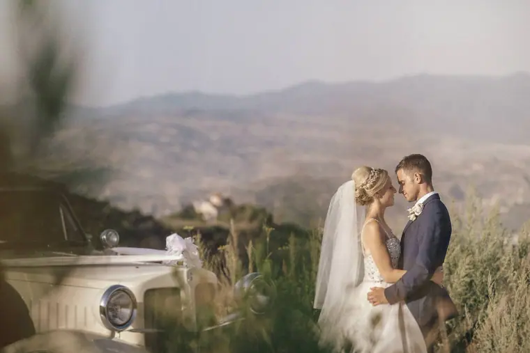 Couple embracing beside the vintage car with misty mountains behind
