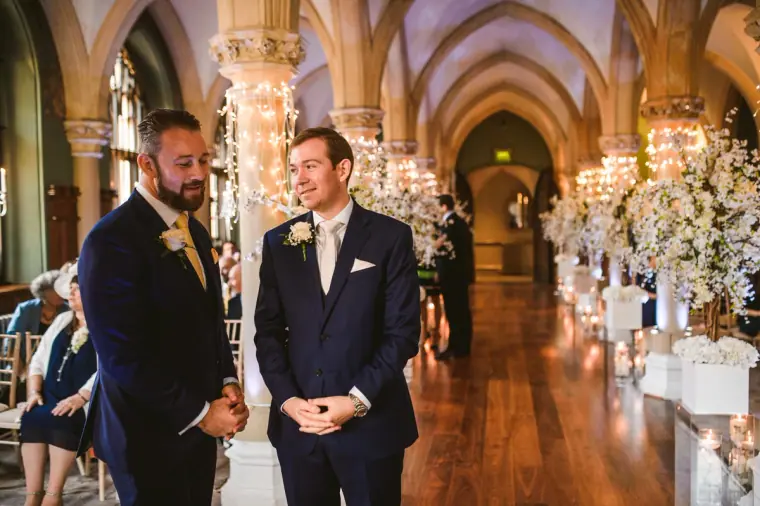 Groom and best man waiting at the front of the blossom-lined ceremony room