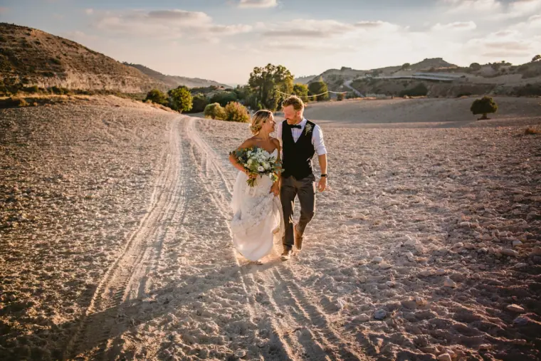 Bride and groom walking hand in hand along a dusty track through the hills