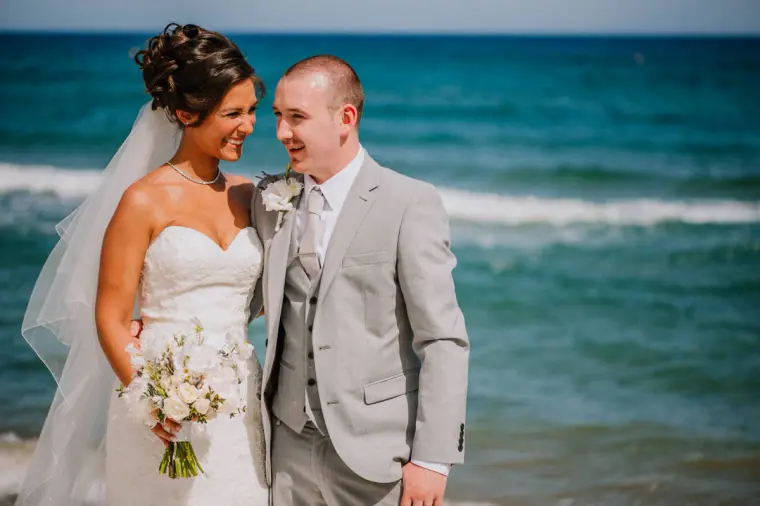 Louise and Mike smiling together on the beach with waves behind them