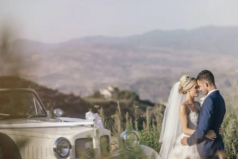 Emmee and Danny touching foreheads beside their vintage car above the hills