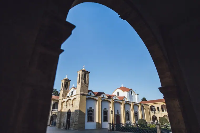 Church bell towers seen through a dark stone archway under blue sky