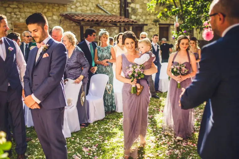 Bridesmaids in lilac walking down the grassy aisle past the waiting groom