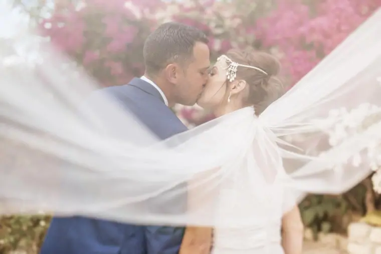 Bride's veil billowing across the frame as the couple kiss