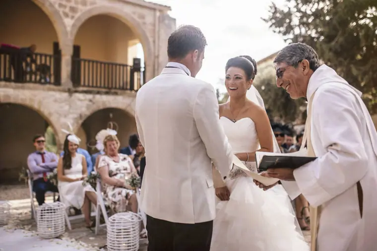 Priest blessing the smiling bride and groom in the arched courtyard