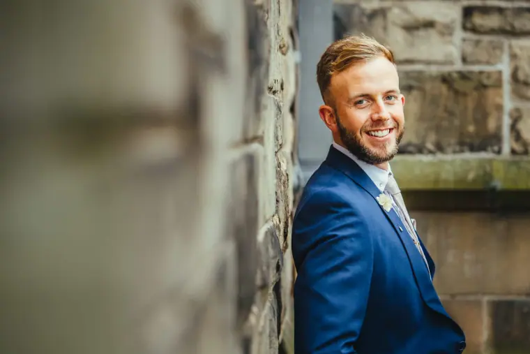 Groom in a blue three-piece suit smiling against a sandstone wall