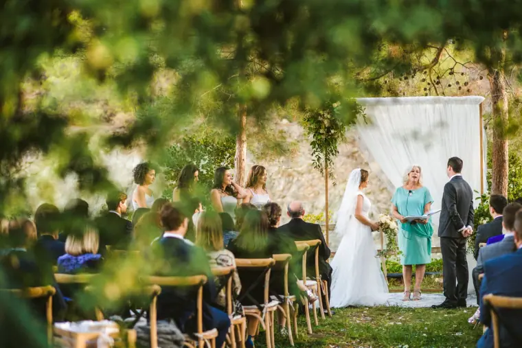 Outdoor ceremony under pine trees at Lexeko Estate with guests seated before a white draped arch