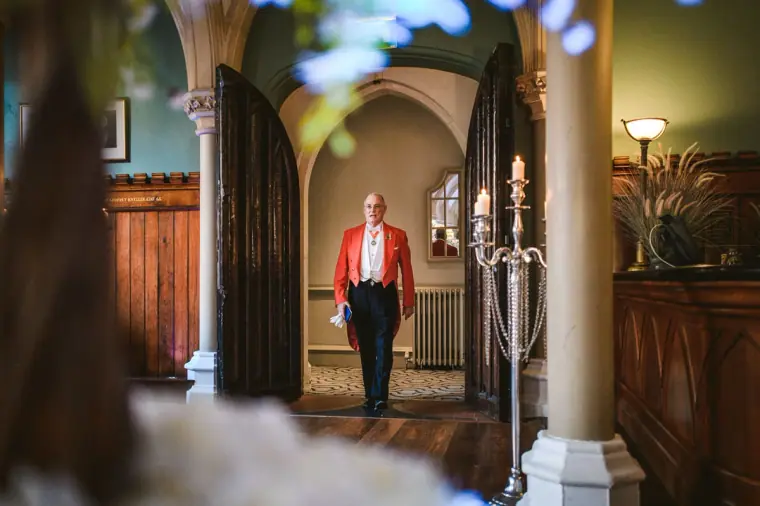 Red-coated toastmaster announcing the bride's arrival through an arched doorway
