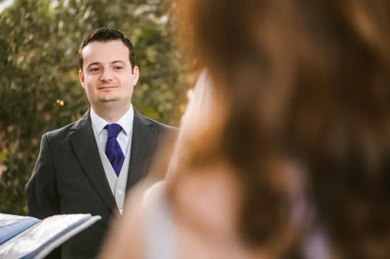 Groom gazing at his bride during the vows, her hair blurred in the foreground