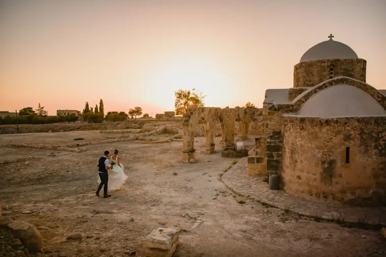 Bride and groom by ruined stone arches and a domed chapel at sunset, Kouklia