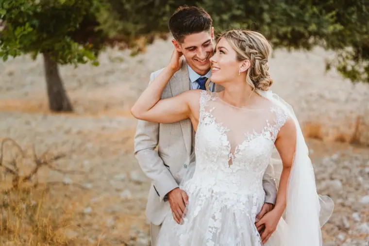 Bride with her arm around the groom's neck in a golden field