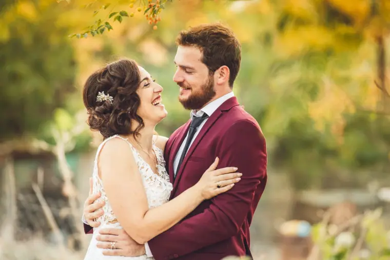 Bride beaming at the groom in his burgundy suit in warm evening light
