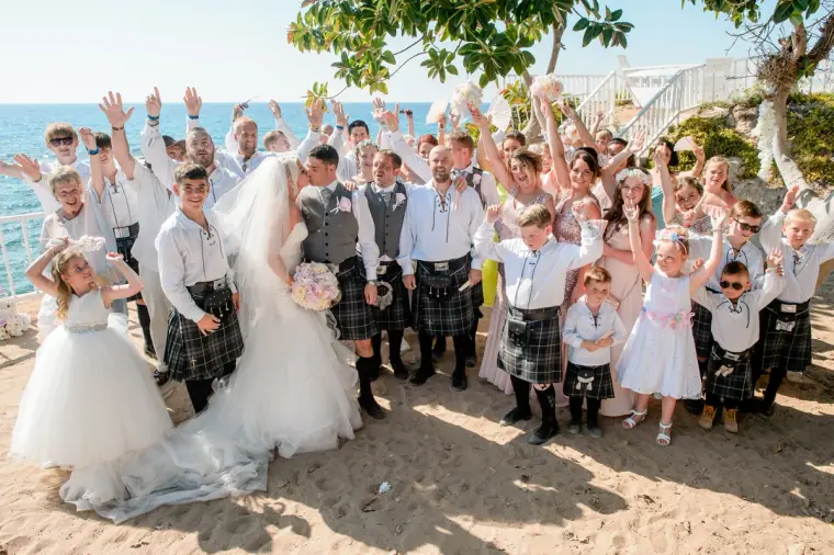 Bride and groom with cheering family and kilted guests arms raised on the sand