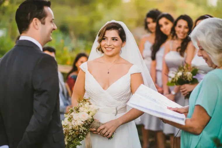 Bride and groom smiling as the celebrant reads beside the bridesmaids