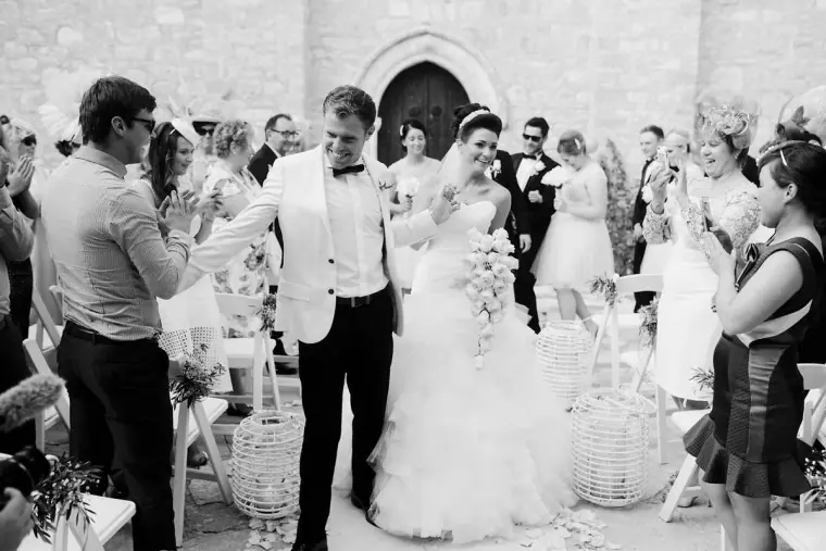 Black-and-white shot of the newlyweds walking back down the aisle as guests applaud