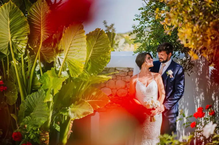 Lauren and Nick embracing among tropical leaves and red flowers at Can Curreu, Ibiza