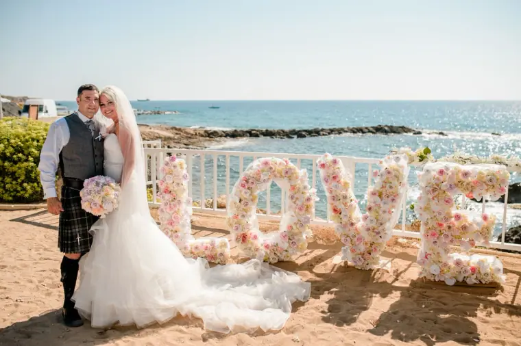 Couple kissing beside a giant floral LOVE sign with the sea behind