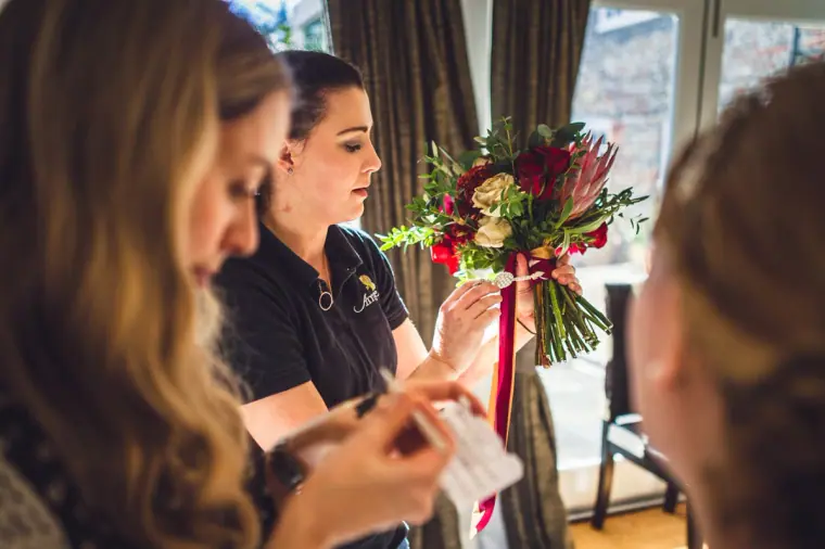 Bridesmaids reading a card beside a red and burgundy bouquet
