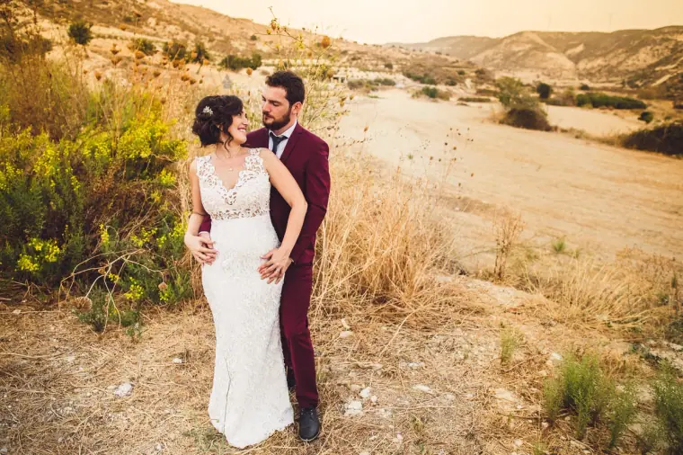 Bride and groom kissing in a dry valley of golden grass in the Paphos hills