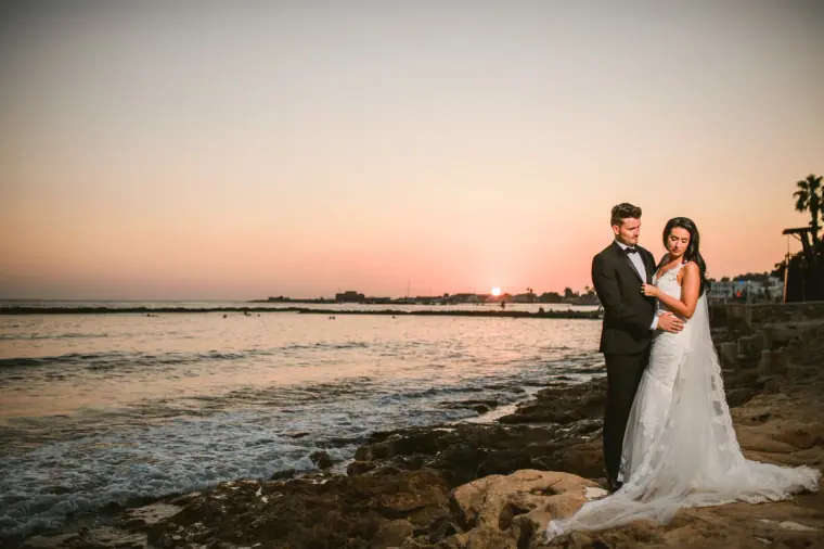 Jaclyn and Steven on the rocky shoreline at sunset, the sea glowing behind them
