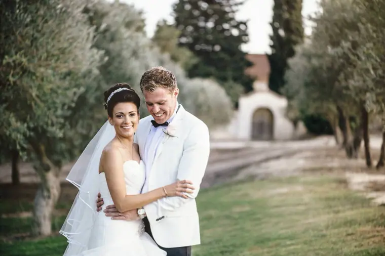 Bride and groom smiling in an olive grove in front of an old gatehouse