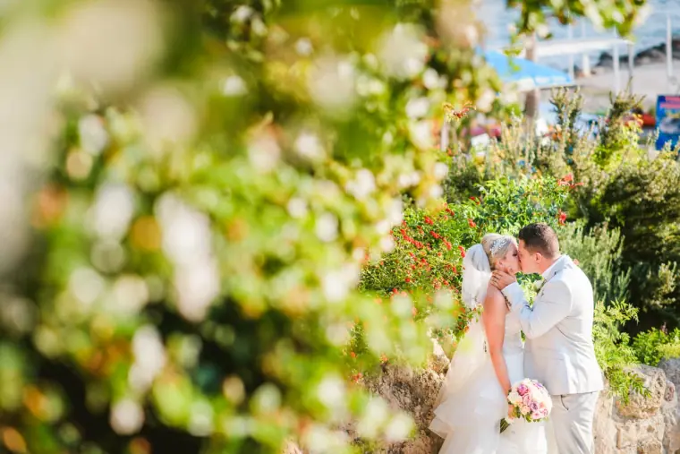 Couple kissing in the hotel gardens, seen through soft-focus leaves