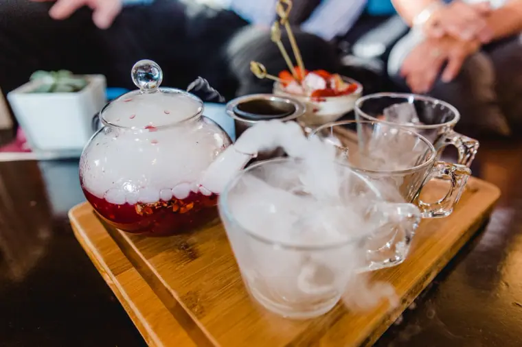 Afternoon tea with a glass teapot and smoking dry-ice cups on a wooden board