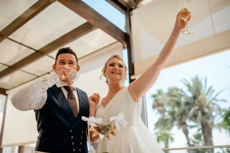 Groom drinking as the bride raises her glass in celebration on the terrace