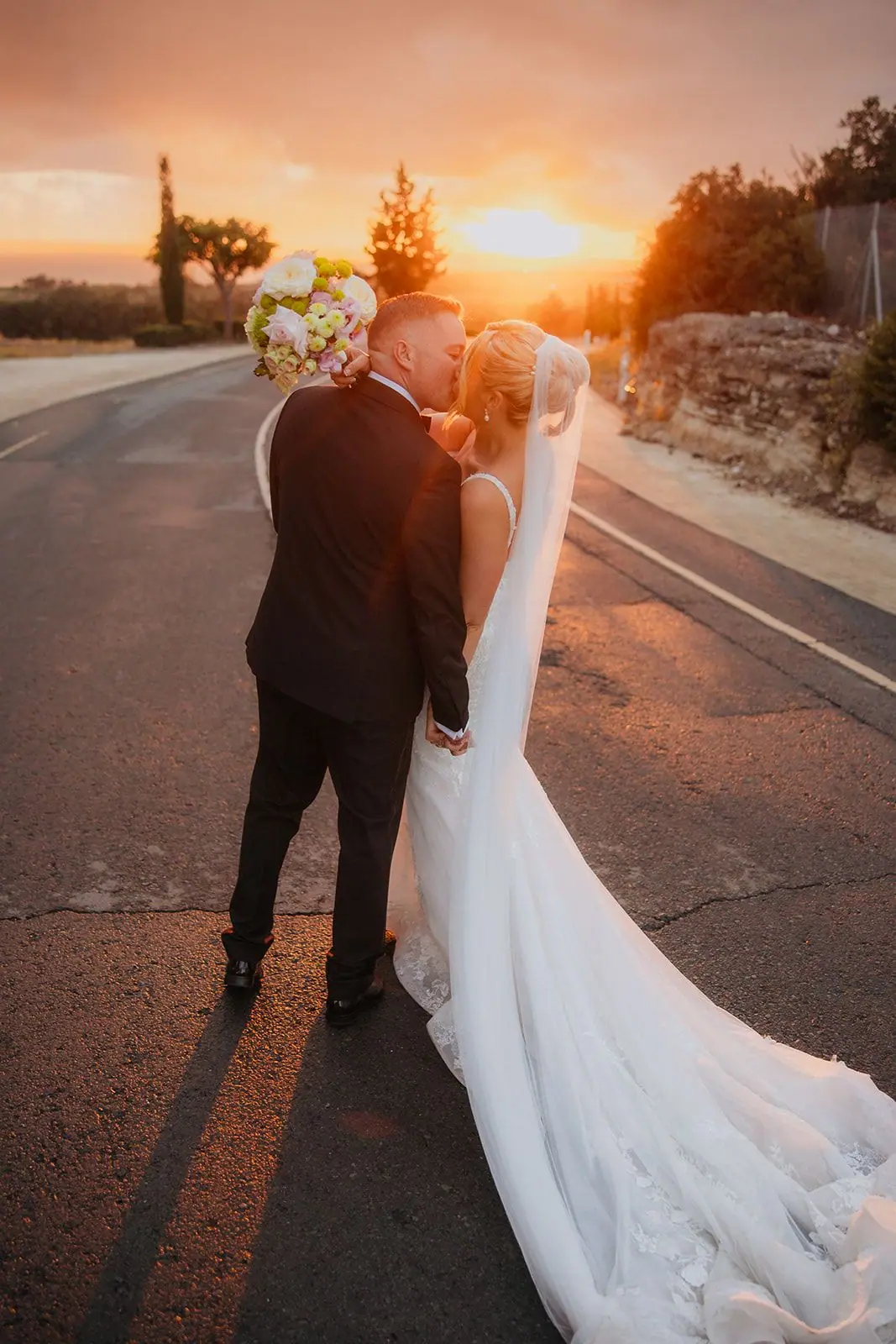 Oliver kissing Zoe on the road as the sun sets, her veil trailing behind