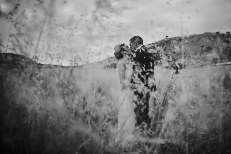 Black-and-white photo of the couple embracing in long grass on a hillside