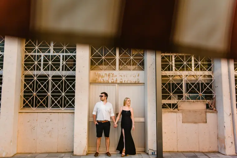 Couple in casual clothes holding hands outside a white building with metal grilles