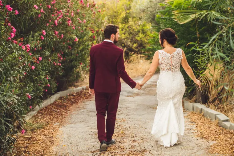 Bride and groom walking hand in hand down a path lined with pink oleanders