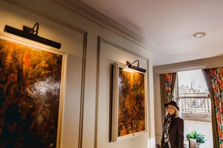 Woman standing by a window in a hotel room hung with large framed paintings