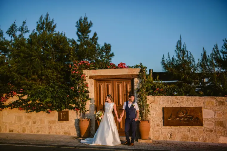 Bride and groom holding hands at the bougainvillea-framed gate of Liopetro, Kouklia