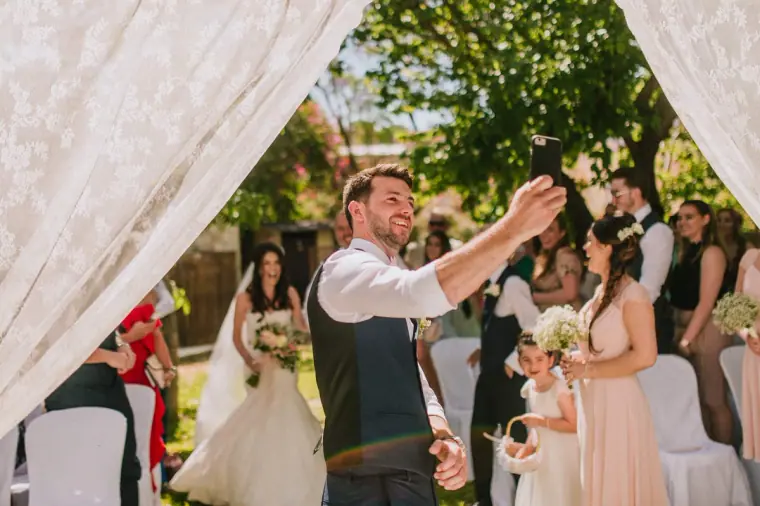 Sean taking a selfie with Claire and the wedding party beneath the lace arch