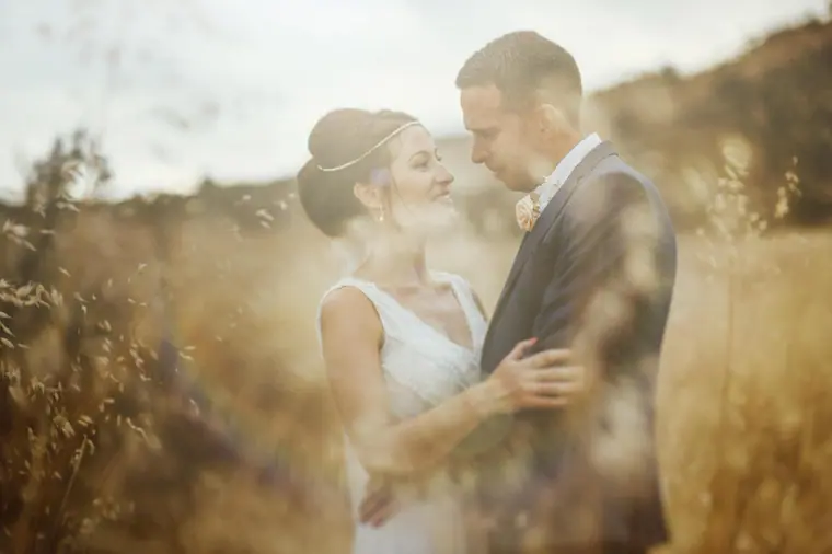 Bride and groom smiling at each other among sunlit golden grasses