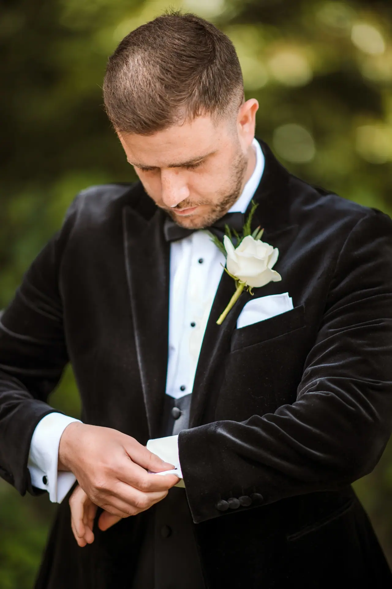 Groom in a velvet tuxedo fastening his cufflinks, white rose buttonhole